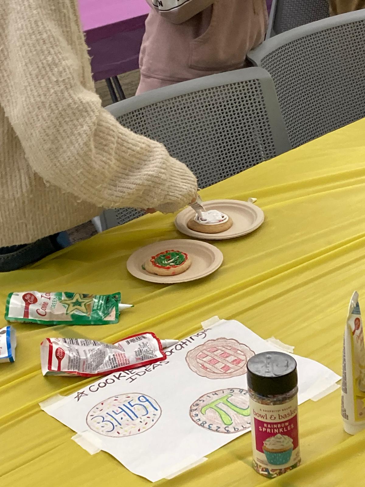 Person decorating circlular cookie, pi day themed decorations on paper